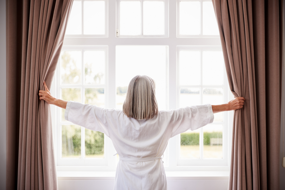 Woman opening up the blinds to look out her window